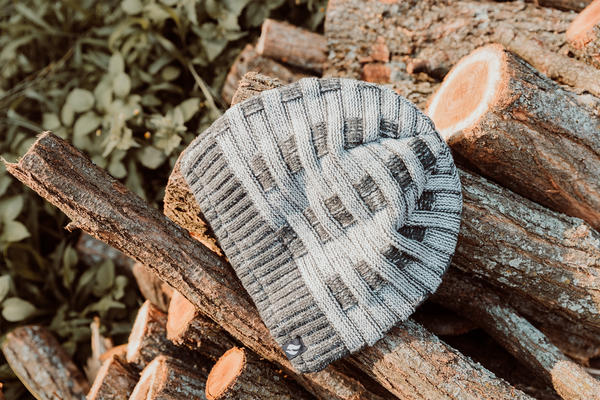 A grey and white beanie rests on some wood in the outdoors. | Heat Holders® | Keep your head warmer this winter.