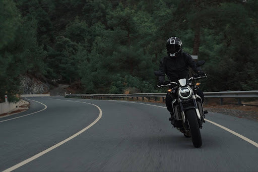  A person riding a motorcycle on a curving road in a forested area. | Heat Holders® The Warmest Thermal Sock®