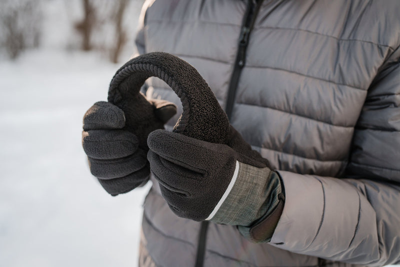Woman wearing a Heat Holders® puffer jacket and gloves, holds Heat Holders® ear muffs in winter