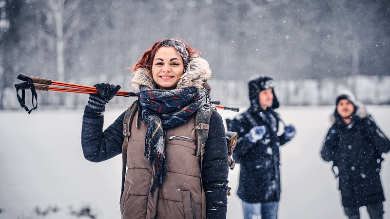 A woman holding hiking poles and two men in the background&nbsp;