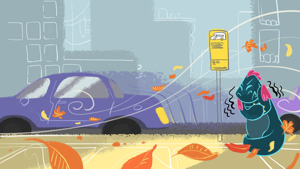 Toestie the Dragon stands shivering at a bus stop in a windy autumn city scene, with leaves blowing around and a car passing by in the background.