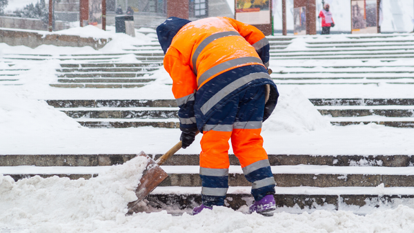  A worker in orange reflective clothing shovels snow from steps during a snowstorm.