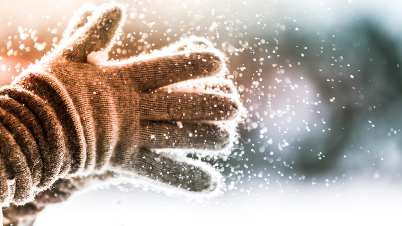 Close-up of gloved hands shaking off snow outdoors.