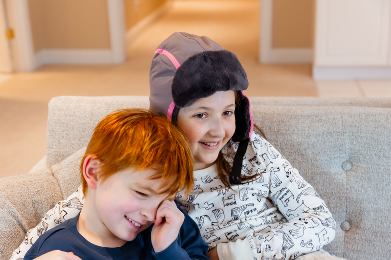 A girl wearing a winter trapper hat cuddles a young boy who is looking sheepish. | Heat Holders®