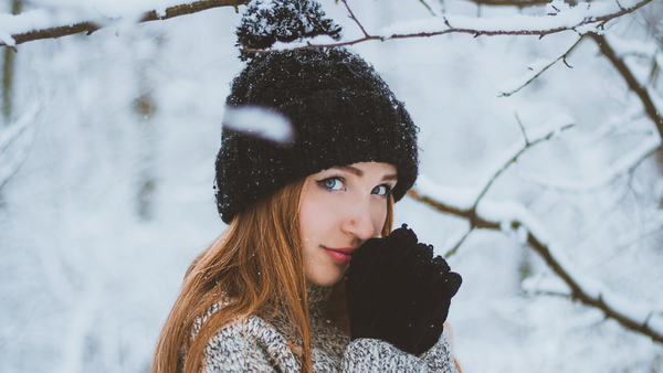 Woman wearing black pom beanie and gloves in a snowy landscape