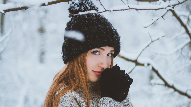 Woman wearing black pom beanie and gloves in a snowy landscape