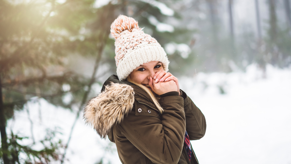 Woman wearing a brown jacket and a pom beanie in a snowy background