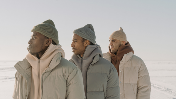 Three men in puffer jackets and knit beanies standing together on a snowy landscape