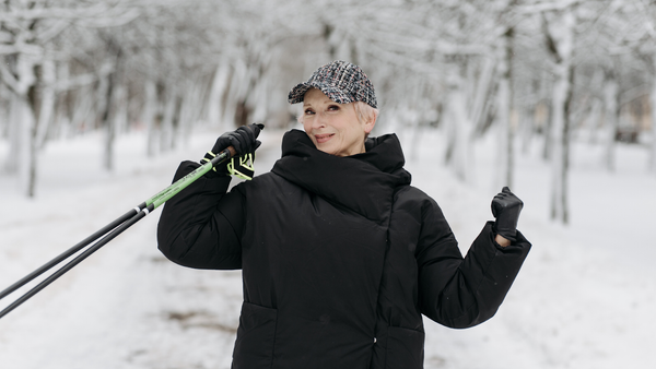 Smiling woman in black coat holding ski poles in snowy park.
