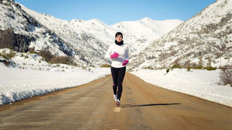 Woman running on a snow-lined road in a mountainous area