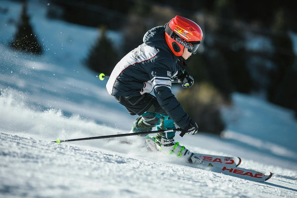 Young skier wearing a red helmet and goggles making a sharp turn on a snowy slope.