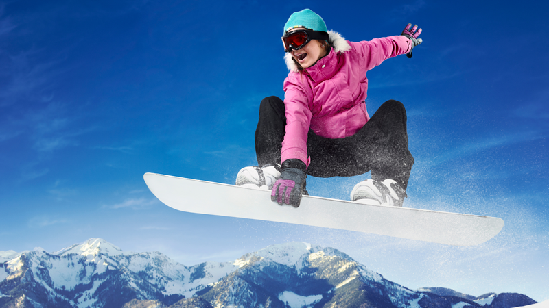 Snowboarder in a pink jacket mid-air against a backdrop of snow-covered mountains