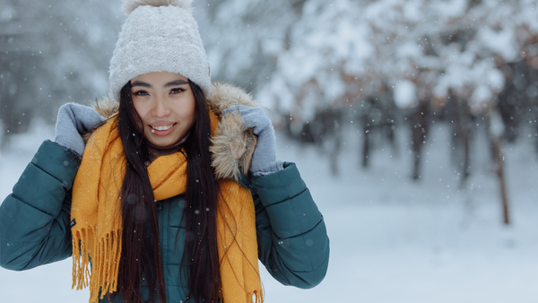 Smiling woman adjusts her jacket in a snowy forest.