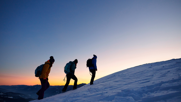 Three people hiking a hill at sunset