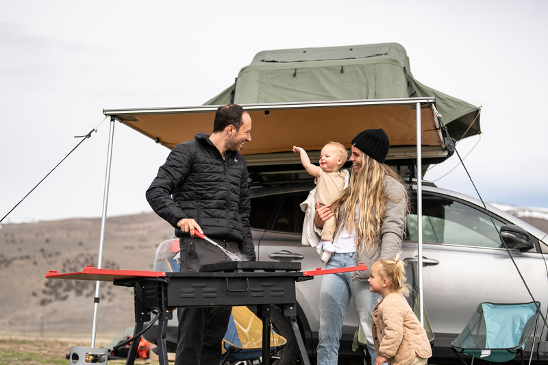 Family enjoying cold camping. Standing in front of their car and raised tent. |Heat Holders®