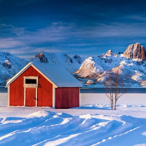 A red house in a field of thick snow, with snowy mountains in the background.