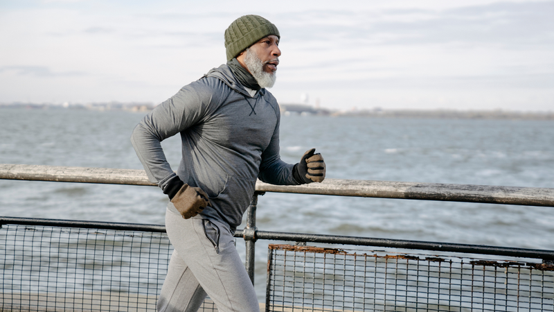 Man in green beanie runs by the water.