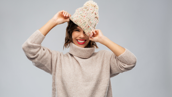 Woman wearing a beige sweater and a cream multi-colored pom hat.