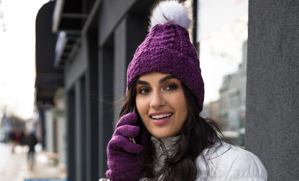 Woman talking on the phone in winter wears Heat Holders® hat with pom pom with matching gloves.